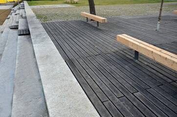 massive bench in the park under a tree in the park urban style beam shape on metal legs in the square. grass grate made of metal and concrete striped tile design with holes for soil grass turf, trunk