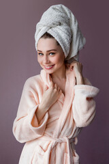 Wall Mural - Arttractive smiling young woman wearing bathrobe and towel over her head standing  over pink background purple background.