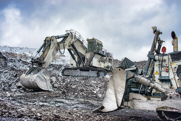 Big excavator and workers in coal mine at cloudy day 