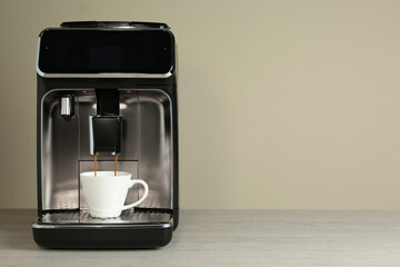 Modern espresso machine pouring coffee into cup on wooden table near beige wall. Space for text