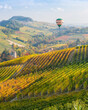 Hot air balloon over the beautiful hills and vineyards during fall season surrounding Barolo village. In the Langhe region, Cuneo, Piedmont, Italy.