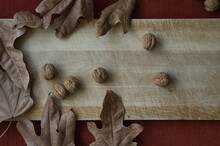 Still Life Of Walnuts With Deciduous Leaves On Wooden Board With Red Background