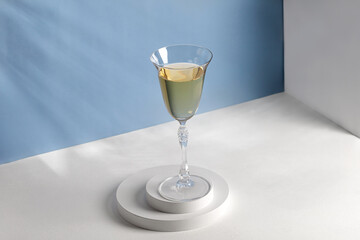 Wine in glass on white podiums. Glass of wine on pedestal in sunlight. Shadow on blue wall.