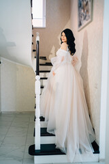 Wall Mural - the bride in a long white wedding dress with a train climbs up the stairs. 