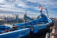 Essaouira, Morocco. October 10, 2021. Small Fishing Boats Moored On Coast At Port Against Cloudy Sky, Wooden Fishing Boats Moored In Harbor