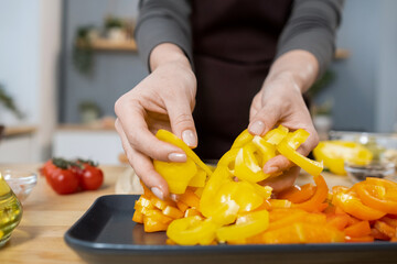 Wall Mural - Hands of female putting chopped fresh yellow capsicum on tray while cooking vegetarian stew for dinner in the kitchen