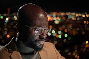 Poster - Young bald businessman in eyeglasses and formalwear standing in front of camera against night traffic lights