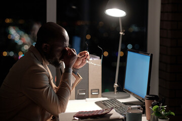 Poster - Young tired businessman touching his face while working in front of computer screen in office late at night