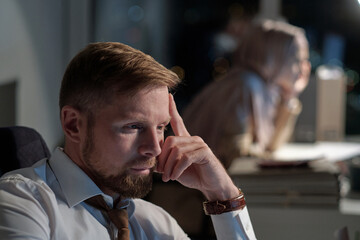 Poster - Serious young businessman in formalwear sitting in front of computer and looking through online data