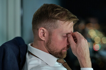Poster - Side view of face of young tired businessman sitting by workplace in office and working overtime at night