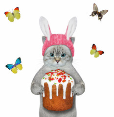 Wall Mural - An ashen cat in a pink easter bunny hat is holding a easter cake. White background. Isolated.