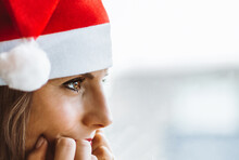 A Light-eyed Woman Wearing A Santa Claus Hat Gazes Pensively At The Horizon Through A Window. Horizontal Banner Format.