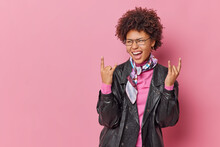 Positive Fashionable Curly Woman Makes Rock N Roll Gesture Exclaims Loudly Enjoys Party Time Favorite Music Shows Heavy Metal Sign Wears Leather Jacket And Kerchief Isolatedover Pink Background