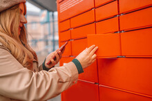 Woman Using Automated Self Service Post Terminal Machine Or Locker To Deposit The Parcel For Storage