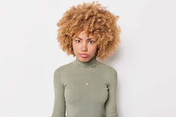 Wall Mural - Portrait of serious young woman has strict angry expression focused at camera dressed in casual jumper poses against white background listens someone attentively analyzes received information