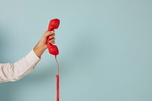 Unidentified Man Holding Red Wired Retro Telephone Handset On Light Blue Banner Background. Male Hand Holds Handset Of Landline Phone Aimed At Free Space For Text. Customer Support Concept.