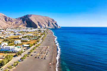 Top view aerial drone photo of black Perissa beach with beautiful turquoise water, sea waves and straw umbrellas. Vacation travel background. Aegean sea, Santorini Island, Greece