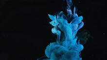 Blue Paint Drops Mixing In Water Slow Motion. Stock Footage. Smooth Ink Swirling And Splashing From Above Underwater Leaving Ink Cloud On Black Background.