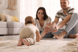 Fototapeta  - Happy parents watching their cute baby crawl on floor at home