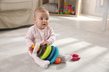 Wall Mural - Cute baby girl playing with toy pyramid on floor at home