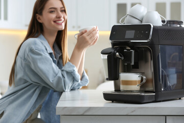 Wall Mural - Young woman enjoying fresh aromatic coffee in kitchen, focus on modern machine