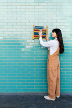 Young Woman Holding Abacus Toy On Turquoise Brick Wall
