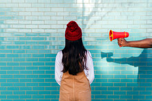 Man's Hand Holding Megaphone By Woman Facing Turquoise Brick Wall