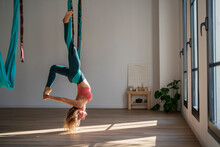 Woman Hanging Upside Down On Aerial Silk Practicing Yoga At Health Club