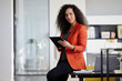© Westend61 - Smiling businesswoman holding tablet PC while sitting on desk in office