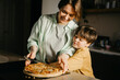 © Westend61 - Son embracing mother holding pizza and cutter at home