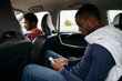 © Westend61 - Young man using smart phone with friends in car on road trip