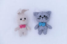 Easter Bunny. Christmas Gift Knitted Handmade Animal Dolls. White Amigurumi Rabbit With Pink Bow Tie And Gray Kitten With Blue Tie. Toys Hare And Cat On White Snow.