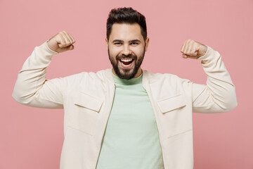 Wall Mural - Young excited happy man 20s in trendy jacket shirt showing biceps muscles on hand demonstrating strength power isolated on plain pastel light pink background studio portrait. People lifestyle concept.