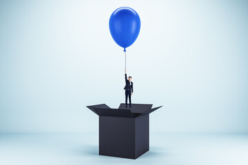 Poster - Abstract image of young european businessman flying on blue balloon out of black paper box on light background. Success, business and happiness concept.