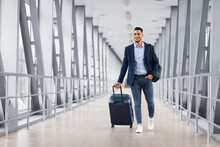Portrait Of Young Middle Eastern Man Walking In Airport Terminal With Luggage
