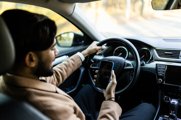 Satisfied young business man with phone in new car