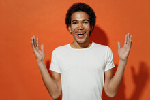 Cheerful Overjoyed Happy Smiling Fun Fashionable Young Black Curly Man 20s Years Old Wears White T-shirt Raise Hands Palms Up Looking Camera Isolated On Plain Pastel Orange Background Studio Portrait.