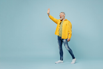 Wall Mural - Full body smiling happy elderly gray-haired mustache bearded man 50s wear yellow shirt walk going waving hand isolated on plain pastel light blue background studio portrait. People lifestyle concept