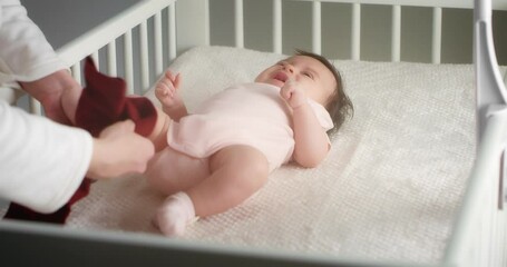 caring mother dresses a newborn baby girl lying on her back in a child crib in beautiful clothes. au