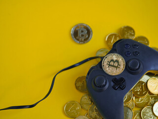 Crypto gaming. Play for earn concept. Top view of a video game controller joystick with focus on a bitcoin cryptocurrency coin on top,  gold coins underneath. Copy space. Vivid yellow background.