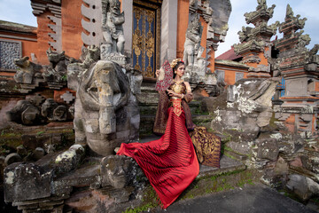Wall Mural - Beautiful balinese girl in traditional costume with a flower and a crown in her hair, and local temple
