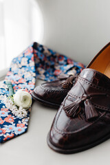 Closeup of elegant stylish male accessories isolated on the white background Side view of groom's leather brown shoes and colorful tie Preparation for wedding Marriage concept Flat lay