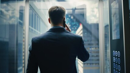 Poster - Successful Businessman in a Suit Riding Glass Elevator to Office in Modern Business Center. Handsome Happy Man Talking on a Phone, Taking an Important Business Call in a Lift.
