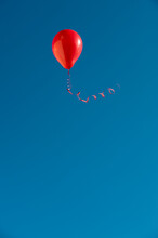 Red Balloon with Ribbon Flying Against Blue Sky