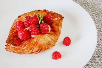 Close up of Raspberry and custard pastry tart on a white dish with two berries on the side