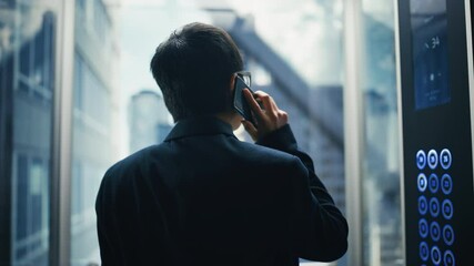 Poster - Successful Stylish Japanese Businessman Riding Glass Elevator to Office in Modern Business Center. Handsome Happy Man Talking on a Phone, Taking an Important Business Call in a Lift.