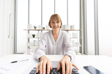 Wall Mural - senior woman typing keyboard on laptop computer, talking and looking to someone from chat online