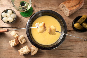 Wall Mural - Fondue from melted cheese with bread on long forks, pickles and wine on a rustic wooden table, traditional new year dish from Switzerland, copy space, high angle view from above