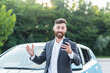 Successful and happy man brags about buying a new car, having fun talking to friends uses a video call in the phone app
