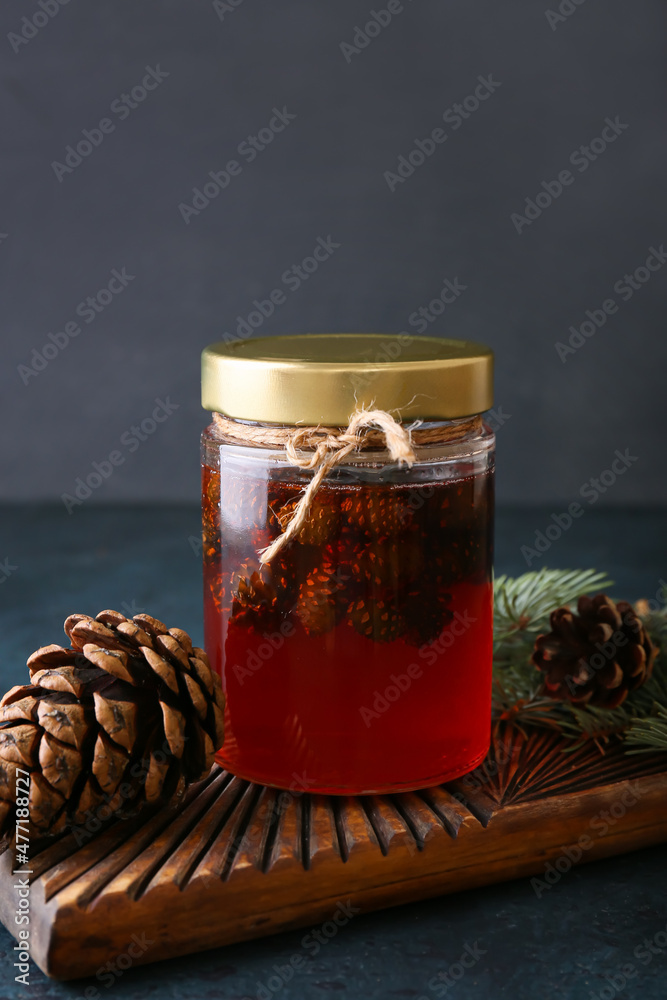 Board with jar of tasty pine cone jam on dark background